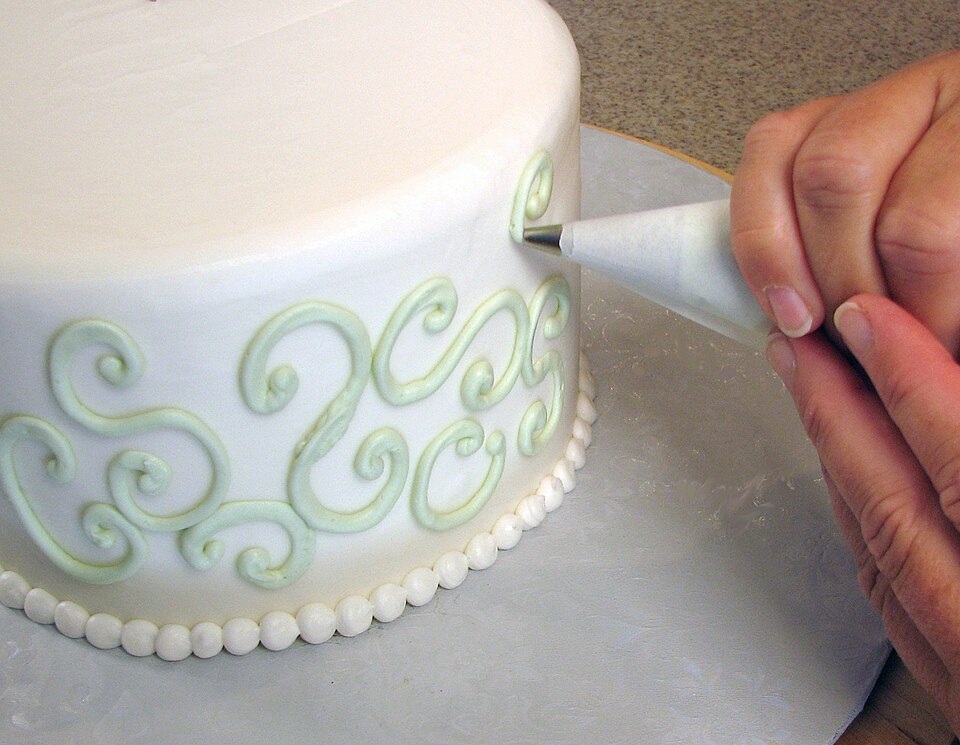 Piping buttercream swirls onto a cake