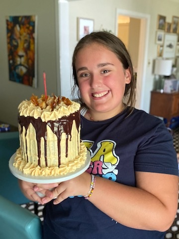 Lelia today, smiling and holding her chocolate and caramel drip cake
