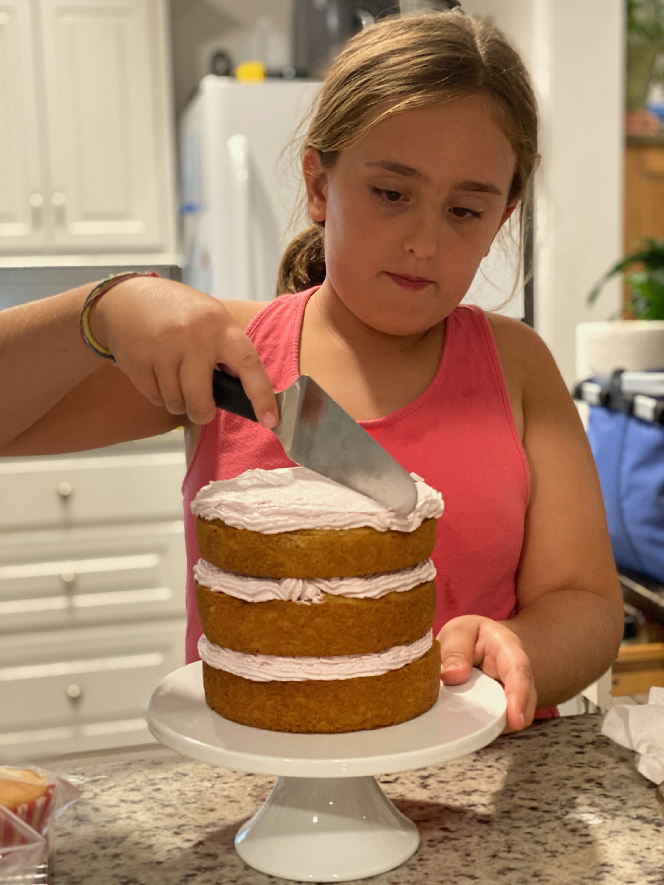 Young Lelia concentrating as she frosts a three-layer cake